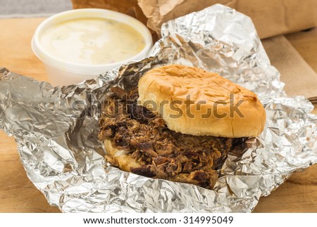 Chopped Barbecue Beef Brisket on bun wrapped in aluminum foil with brown paper bag and order of potato salad.