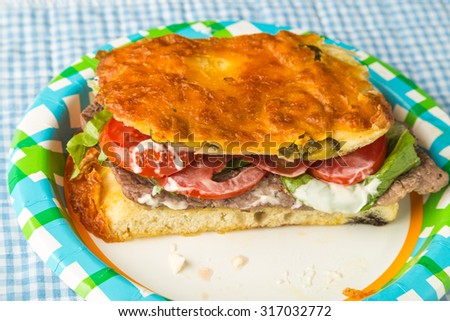 Steak with lettuce, tomato and mayonnaise on Jalapeno-Cheese Focaccia Bread.  Paper picnic plate and blue gingham background.