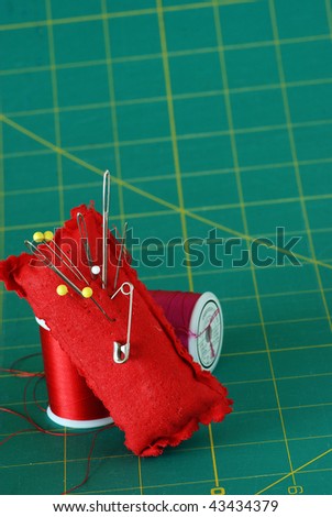 Pincushion and spools of thread with green cutting and measuring board as background.