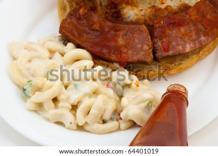 Closeup of barbecue sausage sandwich and macaroni salad with bottle of Louisiana Hot sauce in foreground.