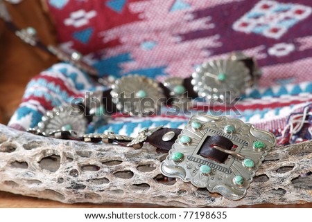 Ornate handcrafted Native American Silver and Turquoise Belt Buckle with leather belt and matching Concho decorations against Navajo blanket background and stick of cholla cactus in foreground.