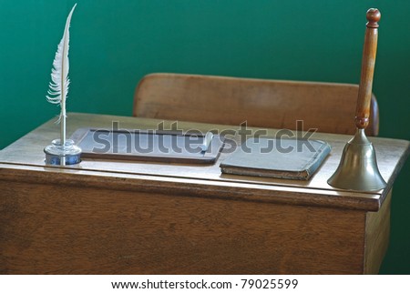Vintage school desk with quill, chalk board and antique bell against green background in dramatic lighting.