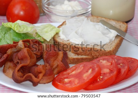 Sliced tomato, fried bacon and lettuce on plate with whole grain toast and mayonnaise.
