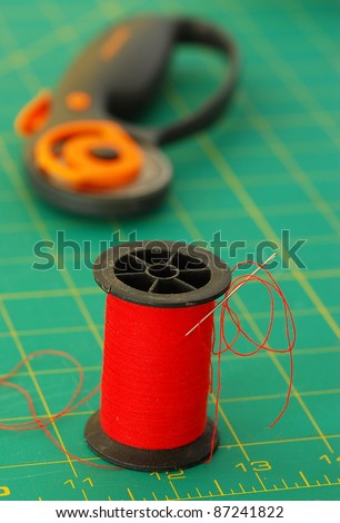 Spool of bright red thread on green cutting pad with rotary cutter in background.  Sewing Still Life.