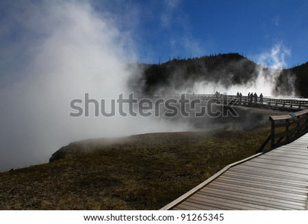 Tourists in silhouette watch mist over thermal pools from boardwalk through Midway Geyser Basin in Yellowstone National Park in Wyoming.