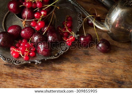 cherry with red currants in a bowl and a metal plate in oriental style on a background of wood.