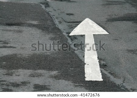 A white arrow painted on damp tarmac