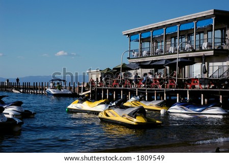 Diners eating at an outdoor restaurant near a jet ski rental business on a lake
