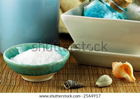 Still life of two bowls of bath crystals, candle, and seashells on a bamboo mat