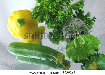 Variety of fresh summer squash pierced with a fork on a reflective watery mirrored background