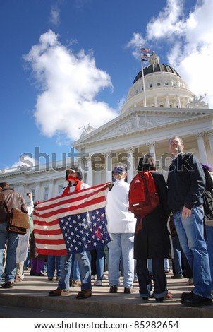 SACRAMENTO, CALIFORNIA - FEBRUARY 26: Protester with mouth covered holds upsdie-down flag at the California State Capitol during rally in Sacramento, California on February 26, 2011