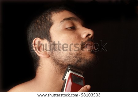 A closeup of a young man trimming his beard with an electric trimmer