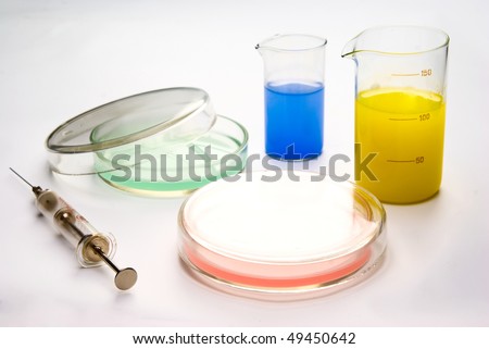 Transparent chemical glassware with green, red, yellow and blue solution with syringe and Petri cup