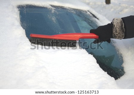 Woman's hand in black garment brushing snow from car windshield closeup
