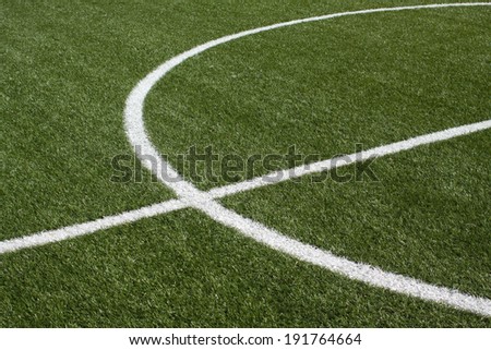 The center part of a soccer field with green synthetic grass and white lines on it closeup.