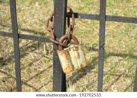 Old rusty metal padlock hangs outdoors on metal fence close up