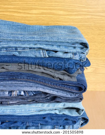 Many folded colored jeans on cupboard shelf, front view close-up