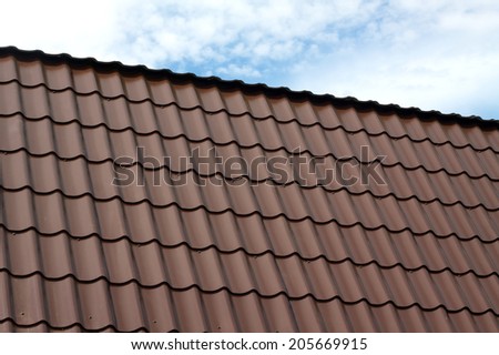 Part of country house roof from brown metal tile under blue sky with white clouds closeup