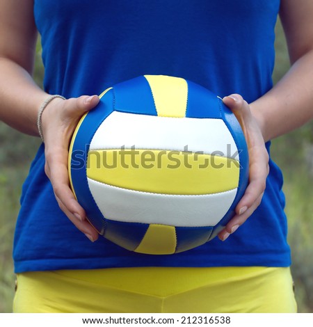 Teenage girl in blue shirt and yellow shorts holding a colorful sports ball for playing volleyball. Closeup Photo