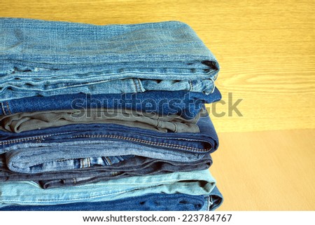 Many folded colored jeans on cupboard shelf, front view close-up