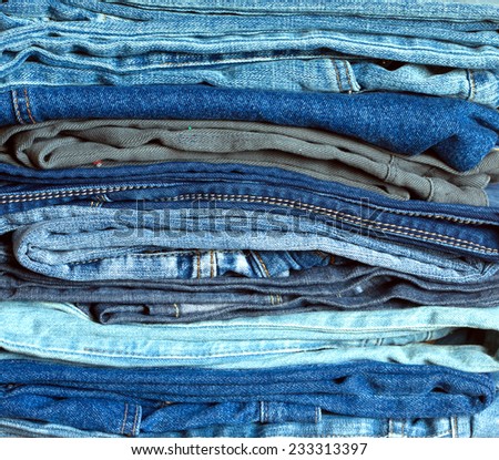 Stack of many colorful folded jeans with double yellow seams, front view close-up