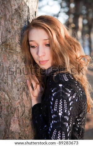 Portrait of blonde girl leaning on the tree in the park