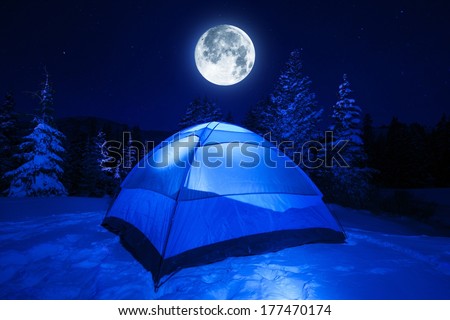 Winter Night Camping in Heavy Mountains Snow. Large Full Moon on the NIght Sky. Outdoor and Recreation Theme.