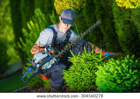 Trimming Works in a Garden. Professional Gardener with His Pro Garden Equipment During His Work. Gasoline Plants Trimmer Equipment.