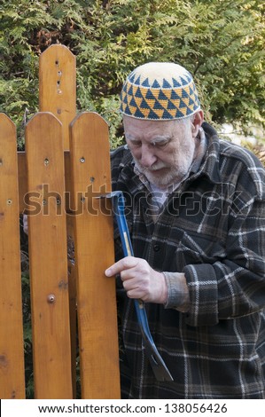 old man with a kufi hat and tool repairing his gate