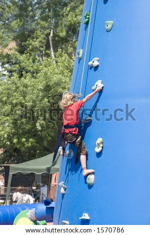Little blondie girl training on an outdoor climbing tower at a fair show held in street of rural country of Quebec, Canada