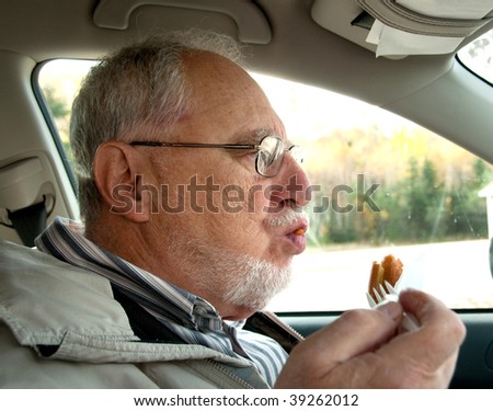 senior man with expressive face,  eating french fries and hot dogs, fast foods in his car