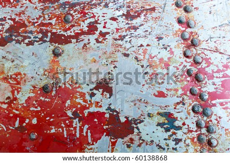 The texture of flaked red paint on metal surface with rivets