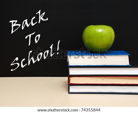 School books with apple on desk, on black school board background