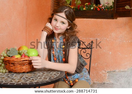 Young girl is sitting at the table with basket of fruits