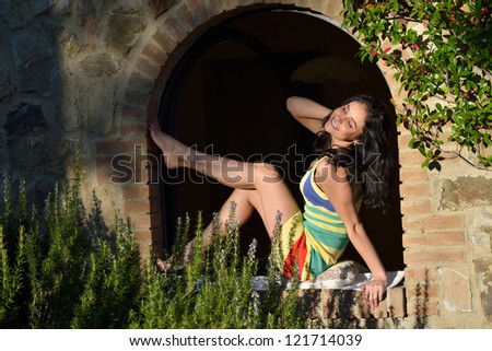 Very beautiful young woman smiling the window of old medieval house in the light of bright sun at early morning