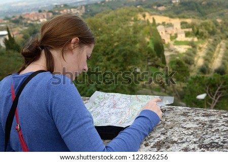 Girl studies tourist map on the stone fence of medieval European city on background of Italian landscape. Italy, Tuscan