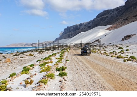 YEMEN - MARCH 11, 2010: Off-road car on the road along ocean shore with big white sand dune, Socotra island. Off-road safari is one of the main local tourist attraction in Socotra