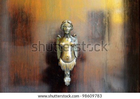 An ancient bronze detail on the old medieval door. A doorknob in form of the naked winged girl