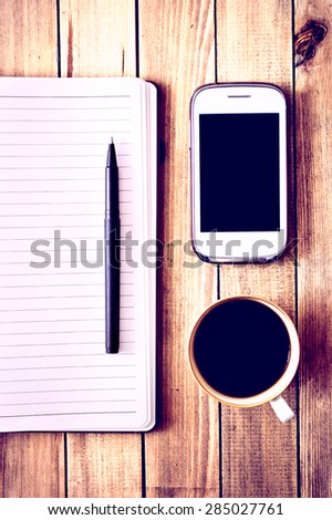 White cell phone, pen, cup of coffee and notebook on wooden table. Work space. Instagram vintage picture.