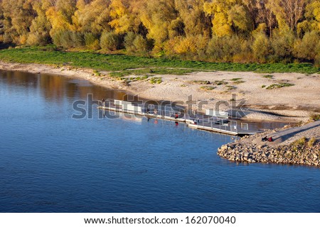 Small pier, beach and autumn trees by the Vistula (Polish: Wisla) river in Warsaw, Poland.
