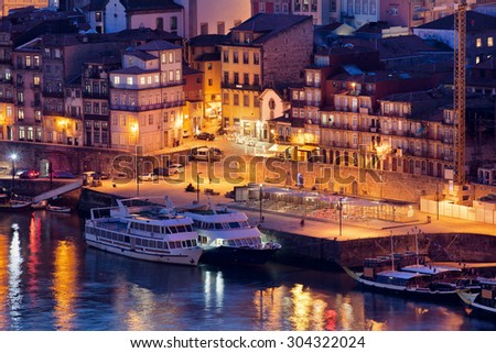 Porto in Portugal by night, houses and cruise boats along Douro river waterfront in historic city centre.