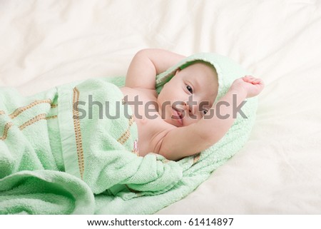 Ten weeks old cute little baby girl wrapped in towel stretching in bed