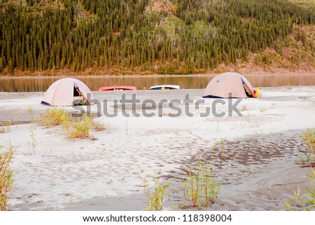 Beached canoes and two tents pitched on a sand bar alongside Yukon River, Yukon Territory, Canada, in remote boreal forest wilderness