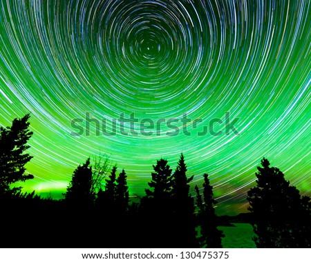 Astrophotography star trails around the Polar Star or Polaris and green glowing display of Northern Lights or Aurora borealis in over taiga forest trees of Yukon Territory  Canada