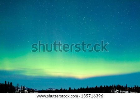 Spectacular display of intense green Northern Lights or Aurora borealis or polar lights over snowy northern winter landscape