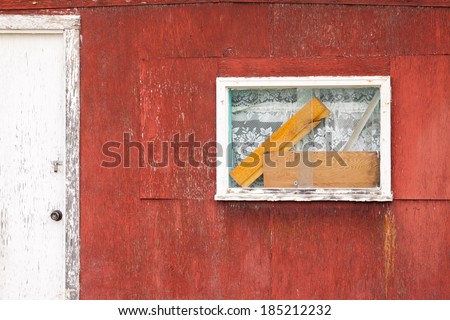 Exterior window on weathered wooden cabin with curtains and blocks of wood behind the glass next to shabby white painted door