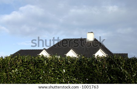 Roof of a house, just appearing over the hedge.