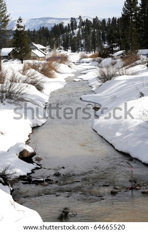 Winter snow bordered stream meanders through mountain community