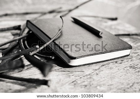Closed black notepad with a pencil laying on a wooden table blurred horizontal black and white