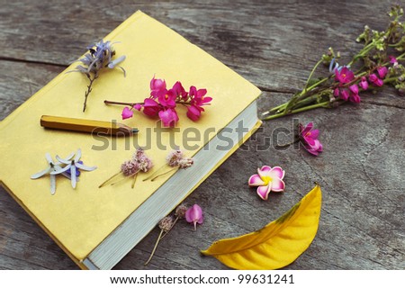 Closed yellow book with flowers and leaves still life on wood table background top view horizontal